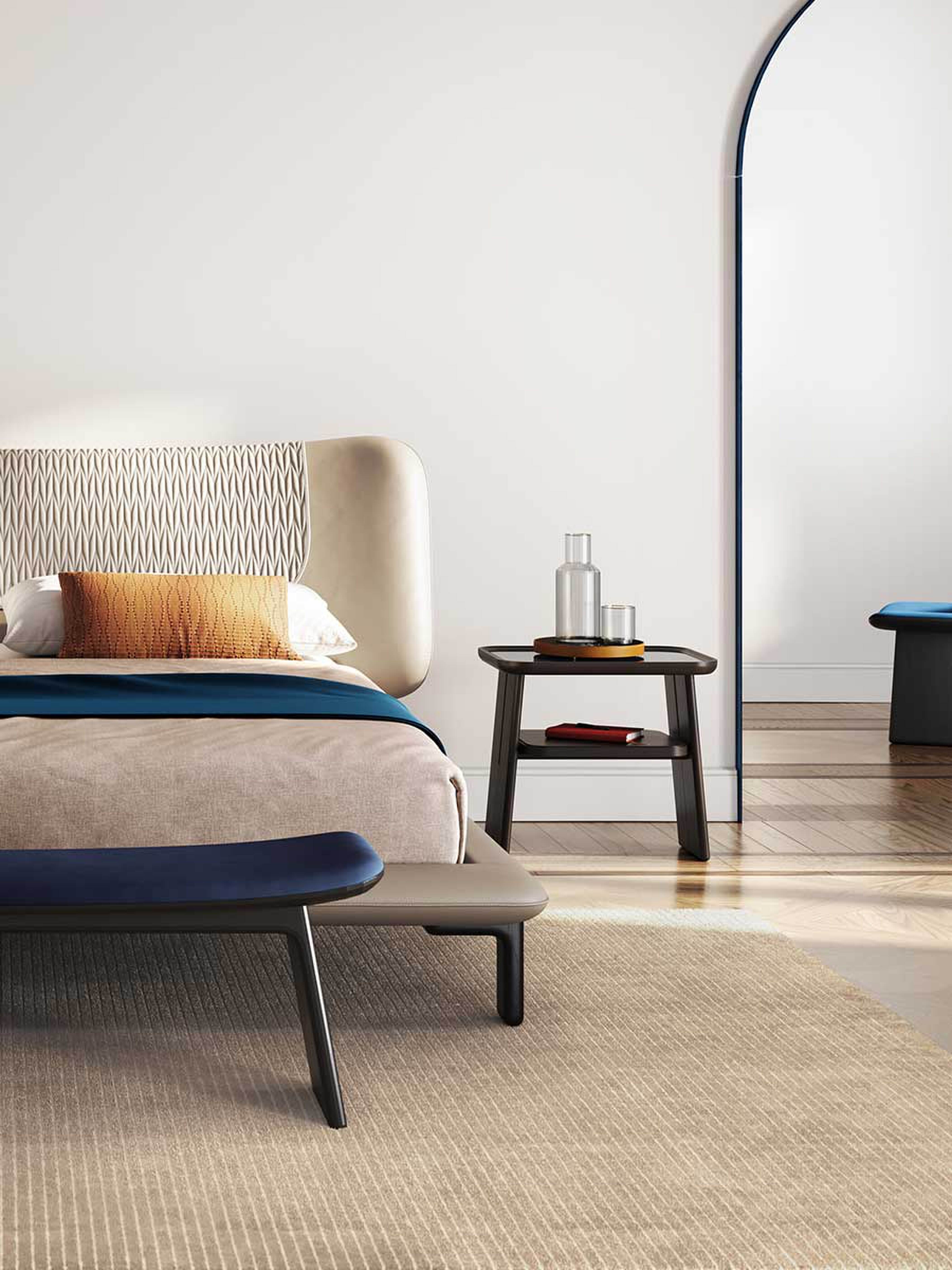 Black nightstand next to a wooden bench at the foot of a bed.